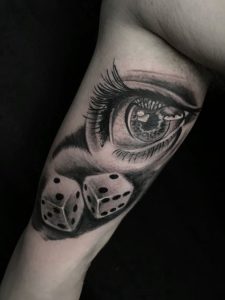 Realistična black and grey tetovaža oka i kocki na bicepsu